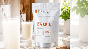 Finally. Casein 500g pouch beside a glass of creamy drink, a scoop and a bowl of protein powder on a kitchen counter.
